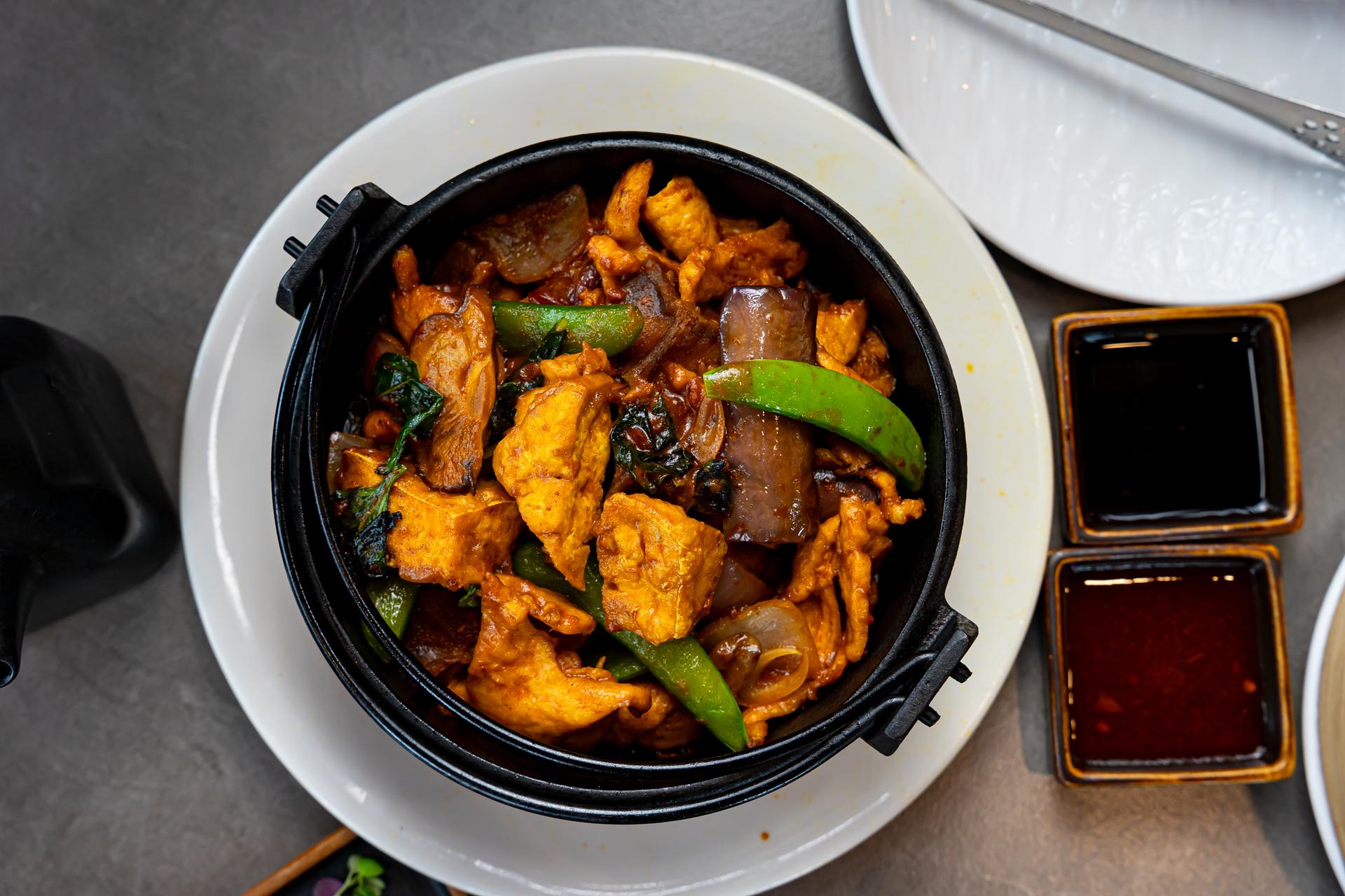 Wok-fired chicken stir-fry with snow peas served in a cast-iron pot